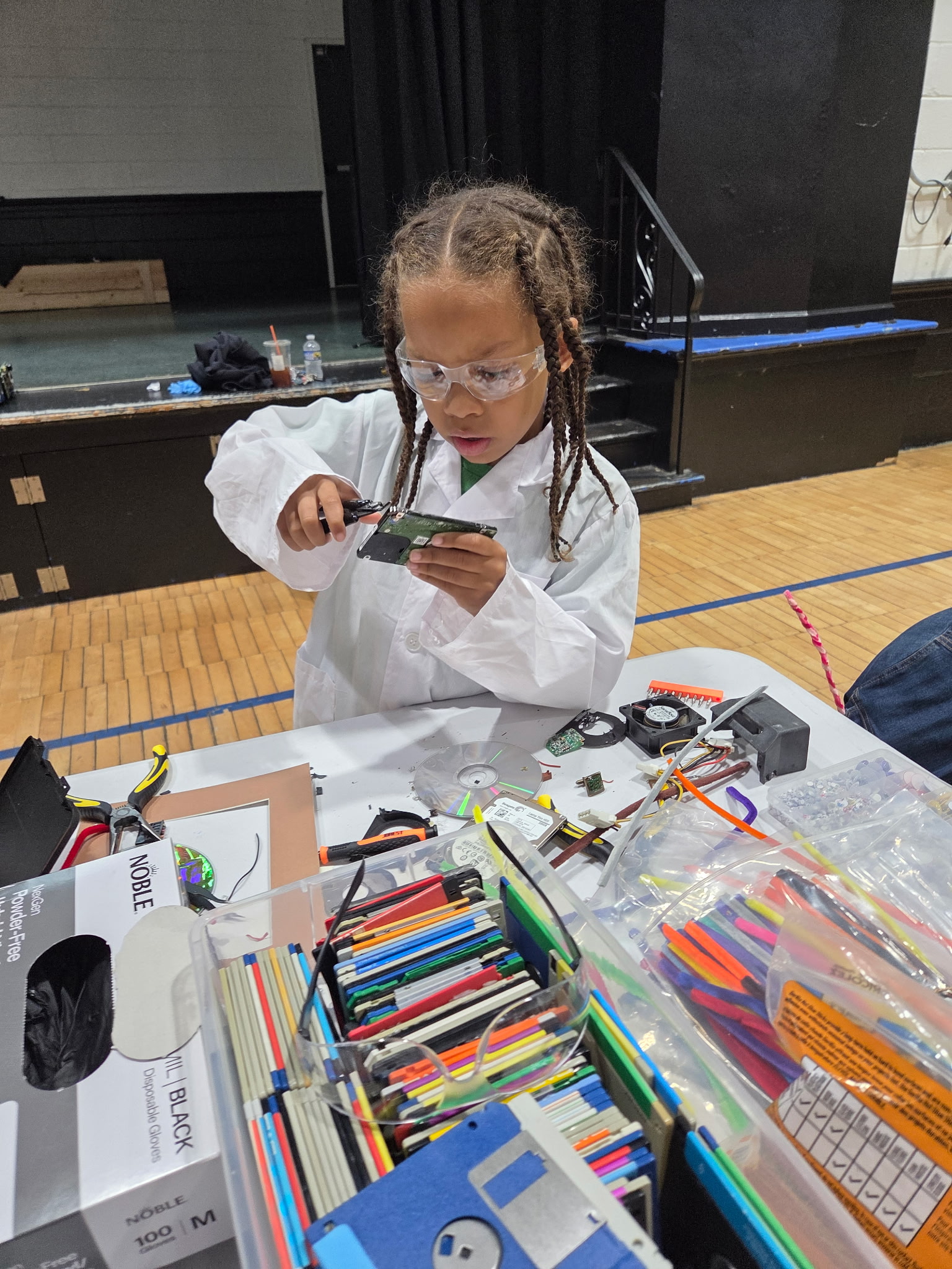 A student holds two hard drive platters up like wheels during a teardown session.