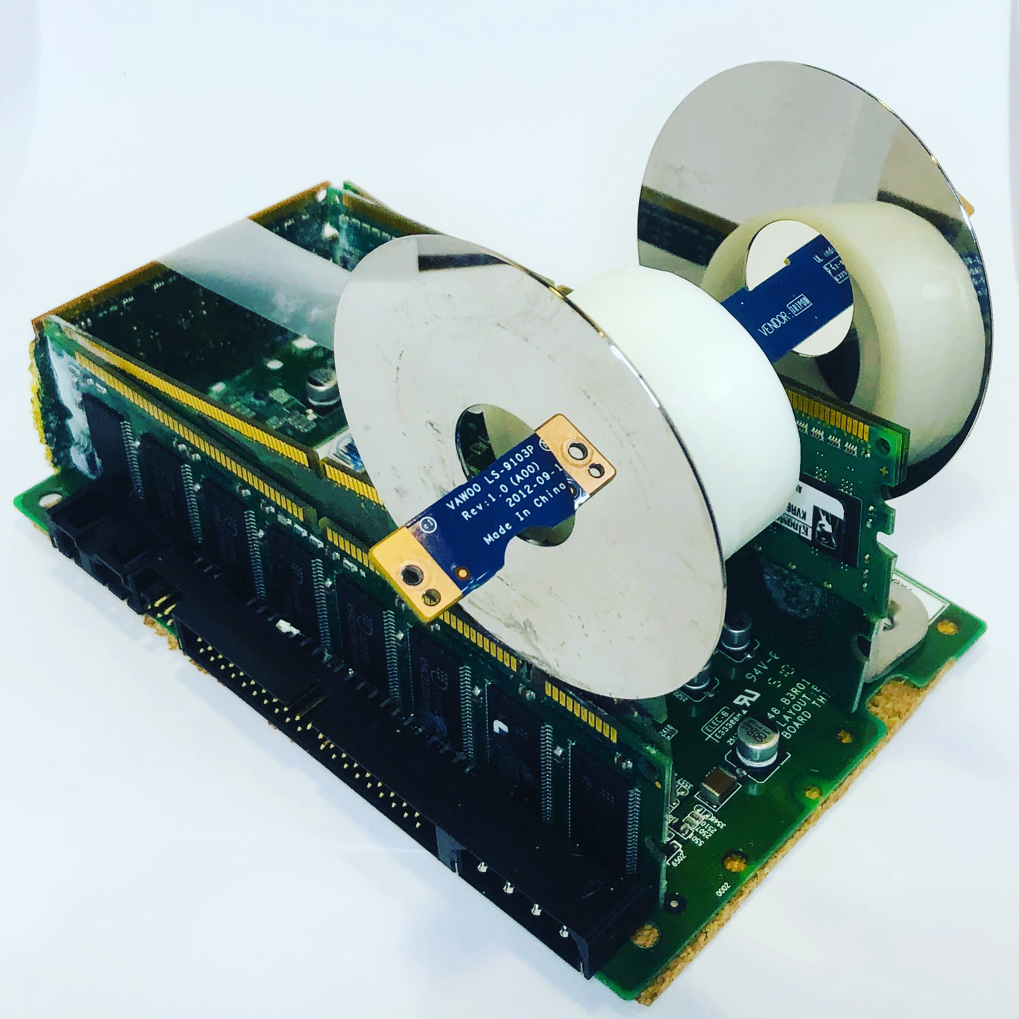 A sculpture built from a green memory board with hard drive platters mounted as wheels.