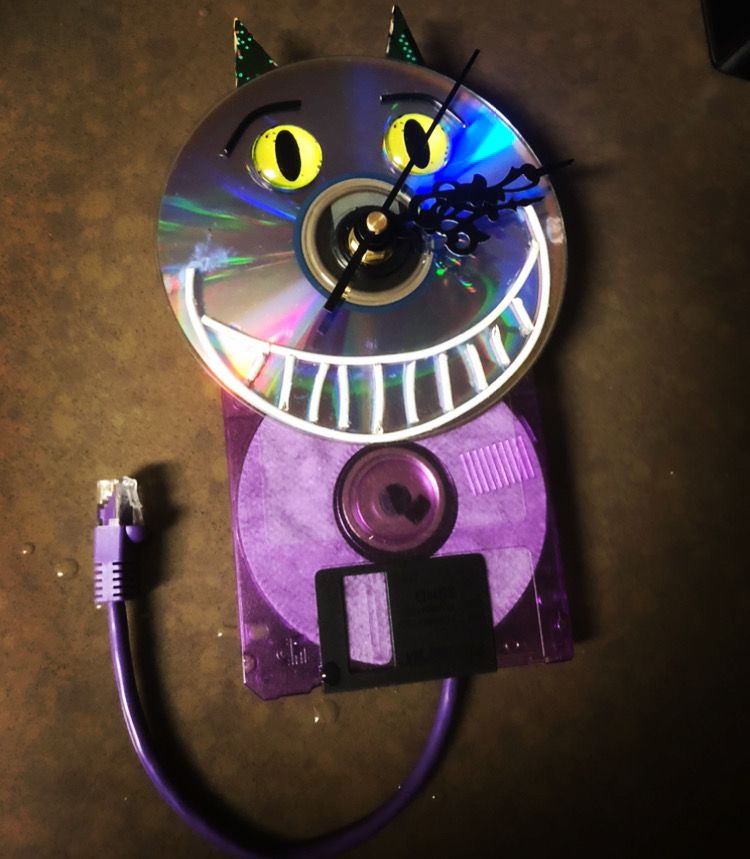 A cat face sculpture made from a CD, circuit board pieces and a network cable tail.