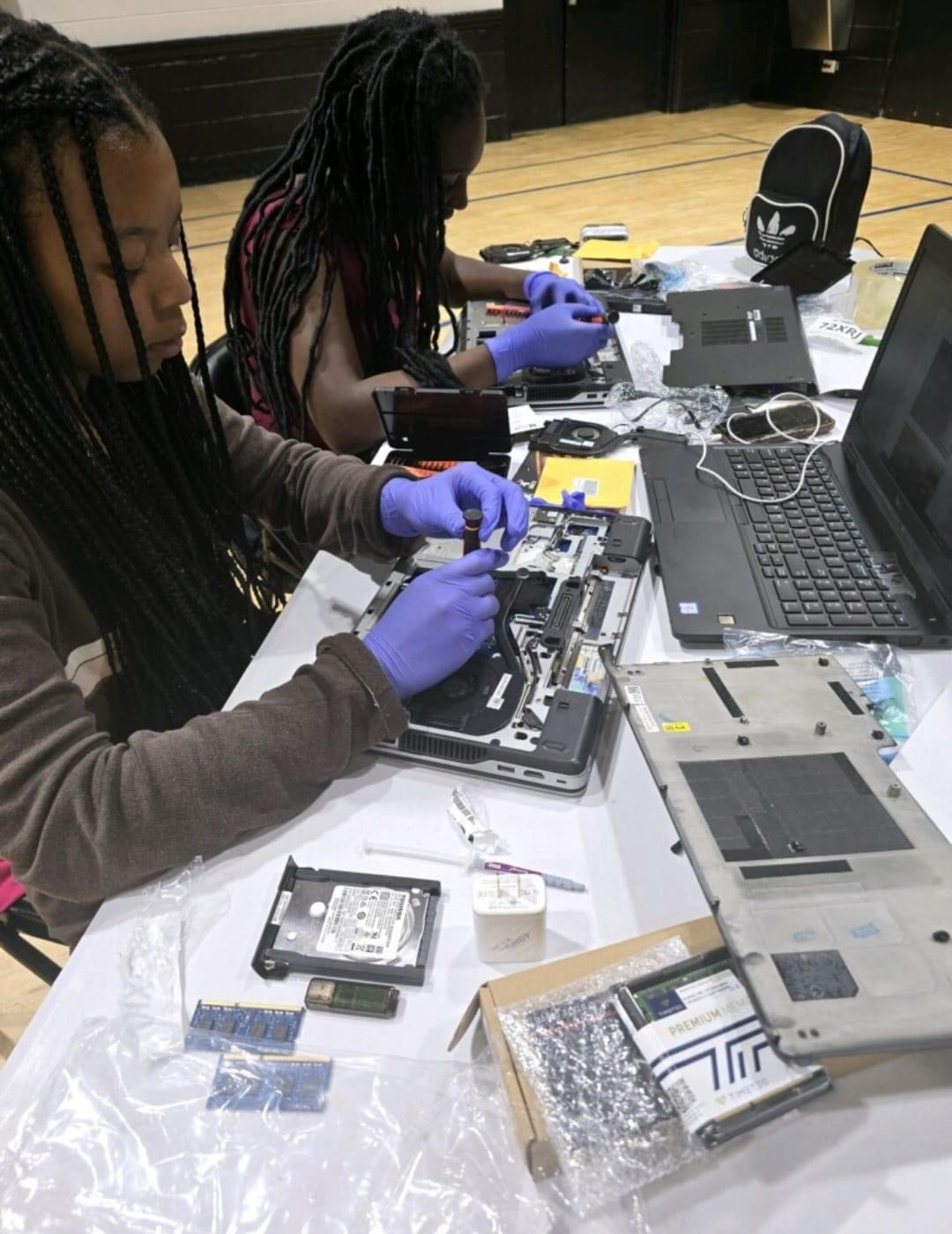 A young student in a lab coat and safety goggles inspects a circuit board pulled from a desktop computer at an eWasteGang workshop.