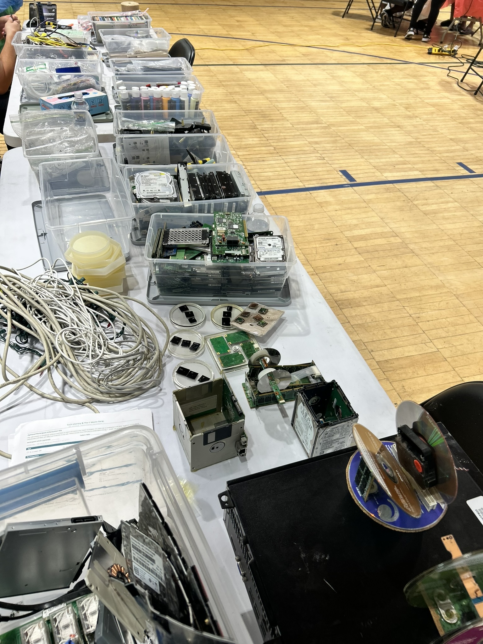 A long table covered in sorted, labelled bins of reclaimed computer components and cables.