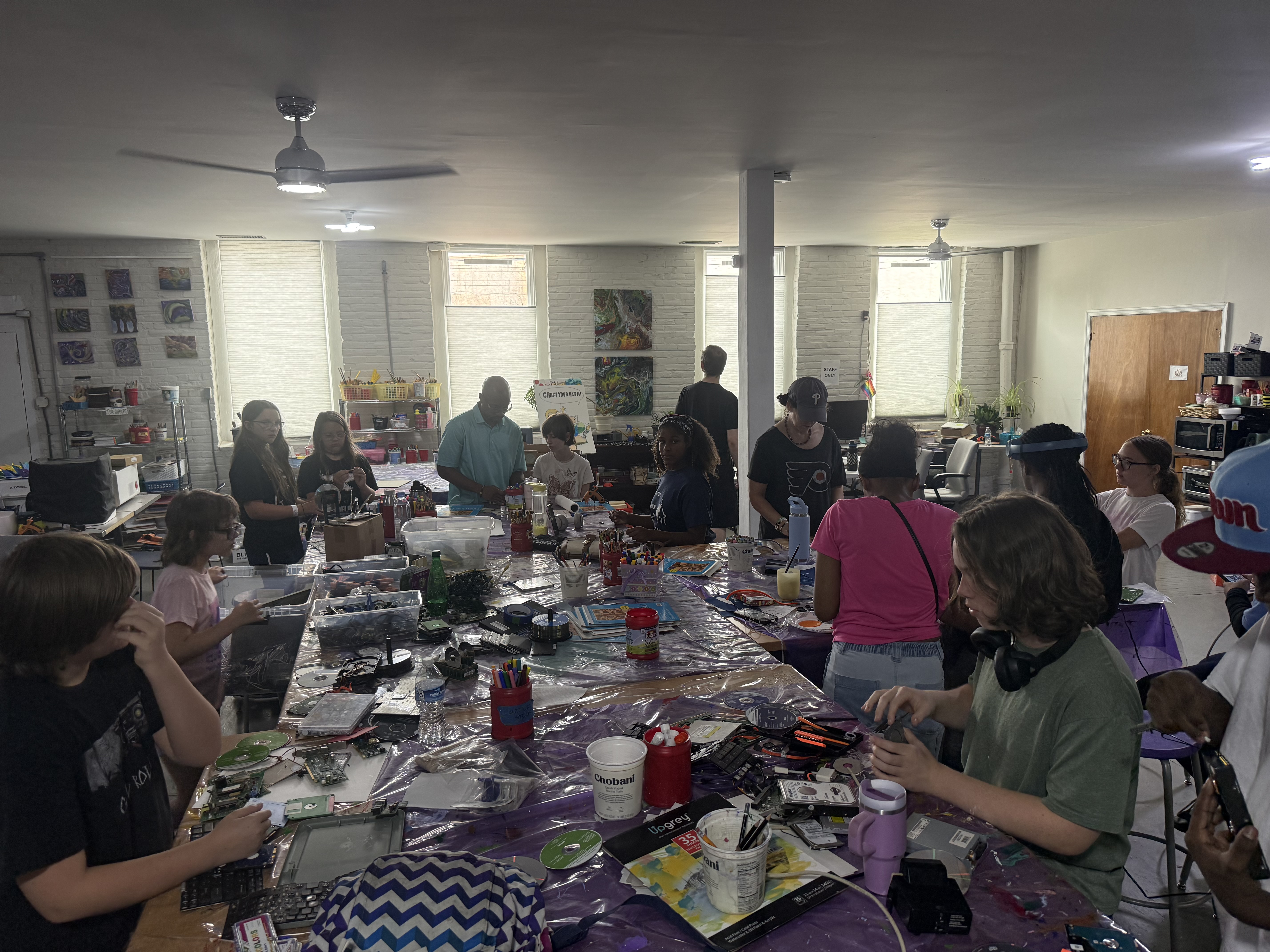 A busy community makerspace with people working at long tables.