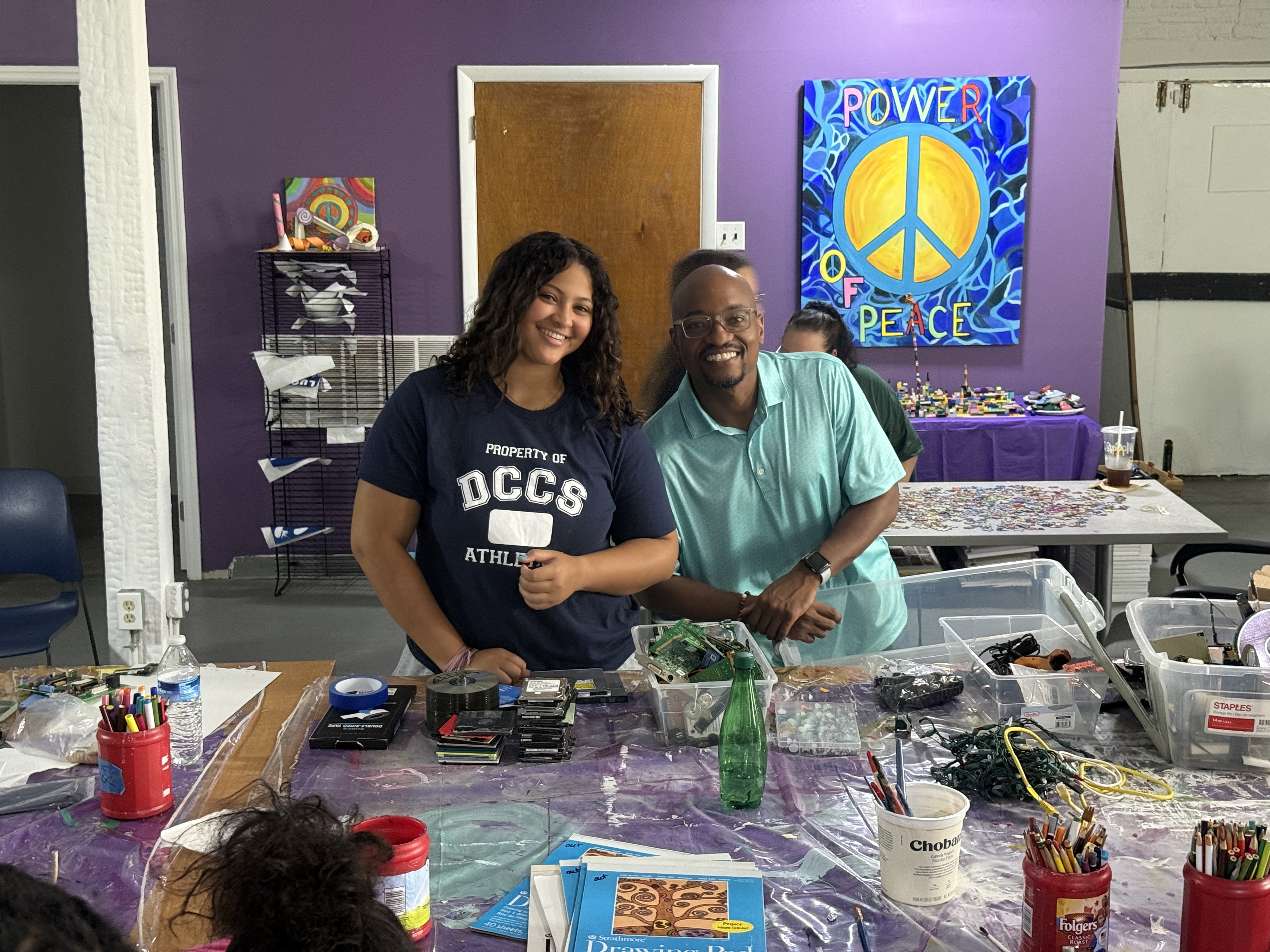 Two community partners smiling behind a table of donated components at a workshop.