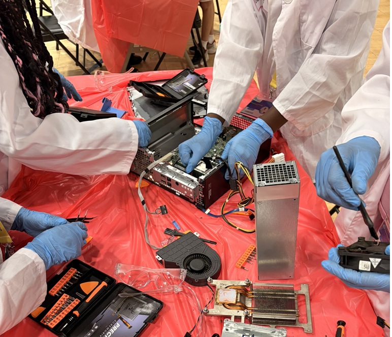 Gloved hands opening a hard drive with a screwdriver, tools laid out on a red workshop table.