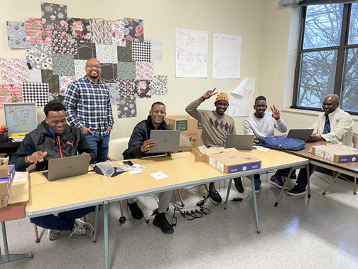 Adult learners at laptops in a classroom, smiling toward the camera.